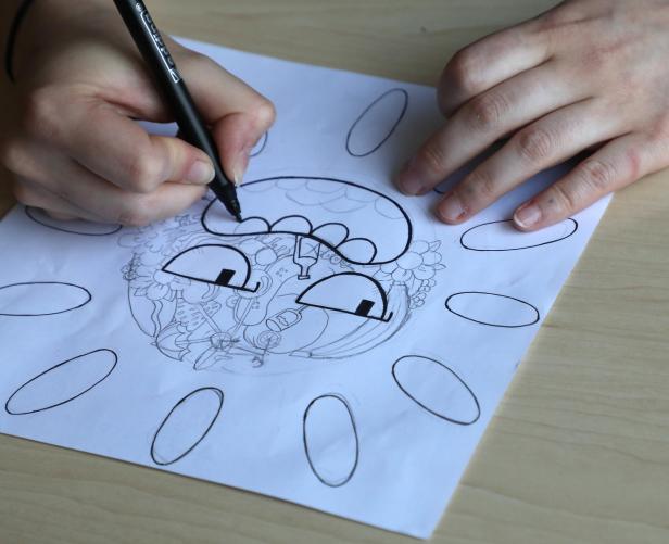 Eine Person zeichnet mit einem schwarzen Stift eine skizzenhafte Illustration auf Papier.