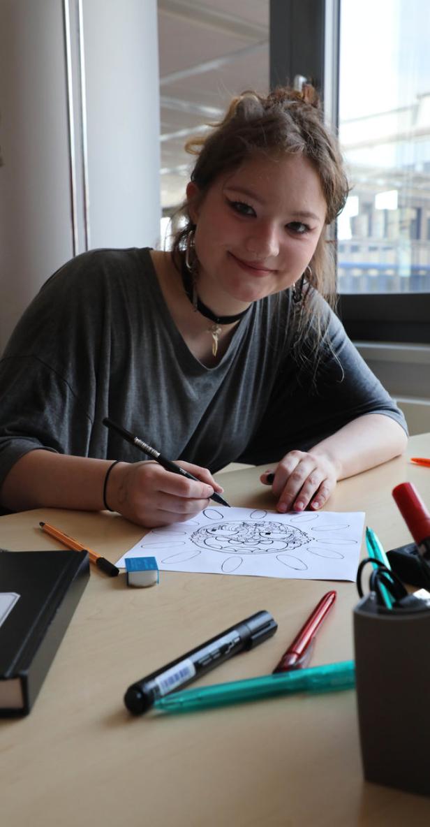 Eine junge Frau zeichnet ein Mandala auf einem Blatt Papier.