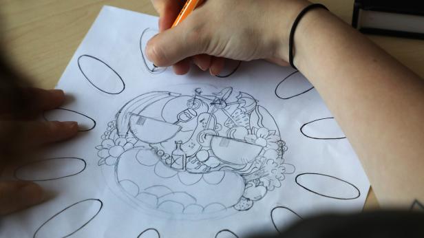 Eine Person zeichnet mit einem Stift eine Illustration mit verschiedenen Objekten auf ein Blatt Papier.