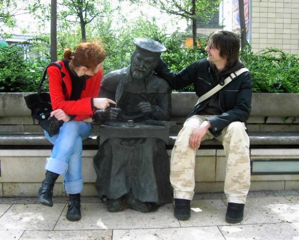 Zwei Personen sitzen neben einer Statue auf einer Bank.
