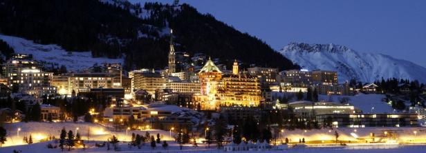 xyz Nachtsicht auf St. Moritz mit beleuchteten Gebäuden und schneebedeckten Bergen.