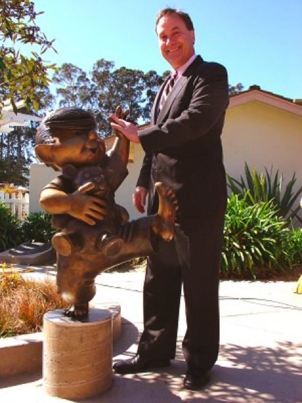 Ein Mann im Anzug gibt einer Bronzestatue eines Kindes ein High-Five.