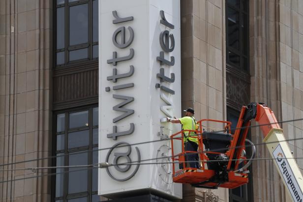 Ein Arbeiter auf einer Hebebühne montiert das Twitter-Logo an einem Gebäude.