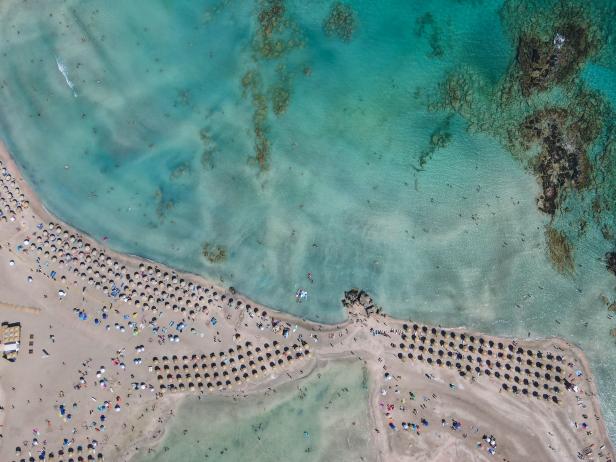 Luftaufnahme von einem Strand mit türkisfarbenem Wasser und vielen Sonnenschirmen.