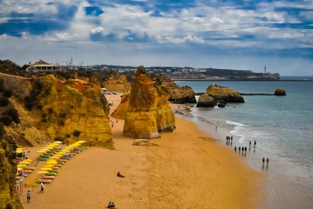 Blick auf den Strand Praia do Camilo in Lagos, Portugal, mit gelben Felsformationen und Menschen.
