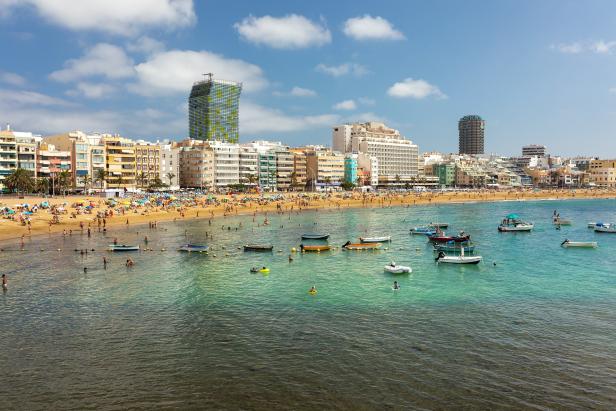 Ein belebter Strand mit vielen Menschen und Booten im türkisfarbenen Wasser.