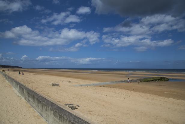 Ein weiter Sandstrand erstreckt sich unter einem Himmel mit weißen Wolken.