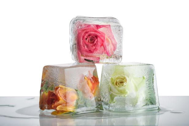 Drei Eiswürfel mit eingefrorenen Rosen in Rosa, Orange und Weiß sind übereinander gestapelt.