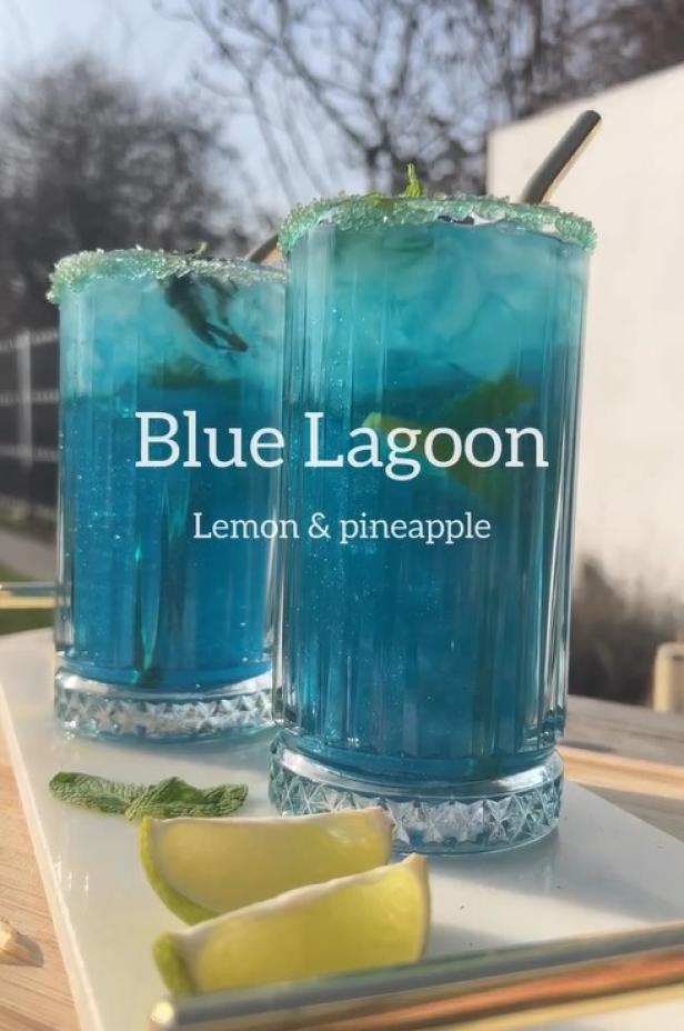 Zwei Gläser mit blauem „Blue Lagoon“-Cocktail, garniert mit Limette und Minze.