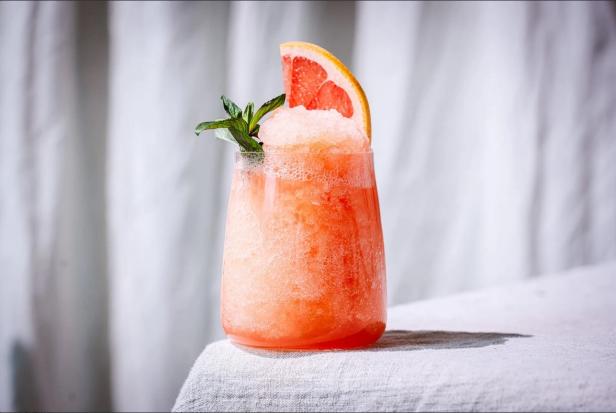 Ein Glas mit einem rosa Cocktail, garniert mit Grapefruit und Minze.