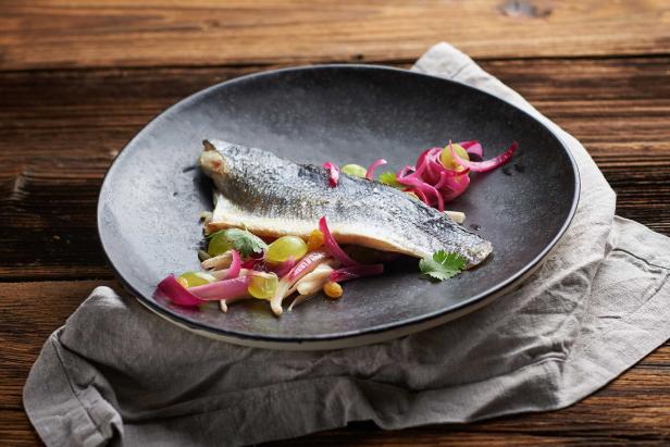 Ein Teller mit gebratenem Fisch, garniert mit Trauben und roten Zwiebeln auf einem Holztisch.