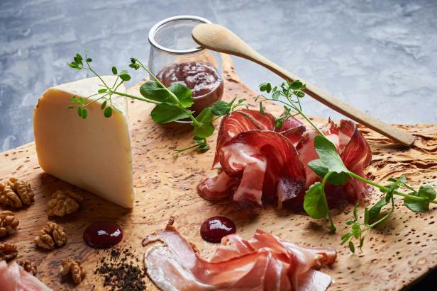 Käse, Schinken, Walnüsse und Marmelade auf einem Holzbrett angerichtet.