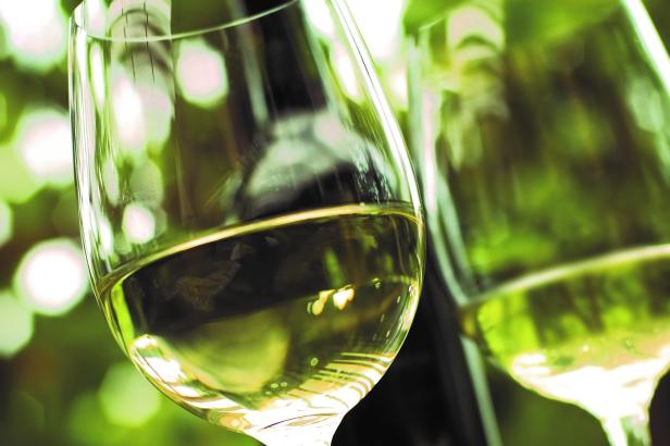 Zwei Gläser Weißwein vor einem verschwommenen, grünen Hintergrund.