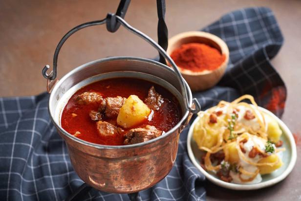 Ein Kessel Gulaschsuppe mit Fleisch und Kartoffeln, serviert mit Beilagen.