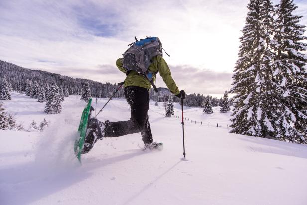Eine Person mit Schneeschuhen und Rucksack wandert durch eine verschneite Winterlandschaft.