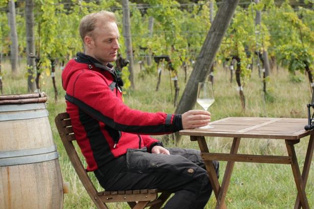Ein Mann sitzt mit einem Glas Wein an einem Tisch in einem Weinberg.