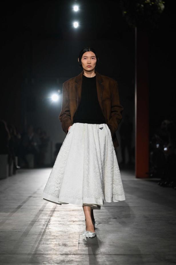 Eine Frau in einem braunen Blazer und einem weißen Prada-Rock auf einem Laufsteg.