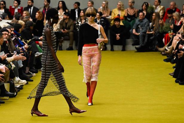 Zwei Models präsentieren Mode auf einem gelben Laufsteg vor Publikum.