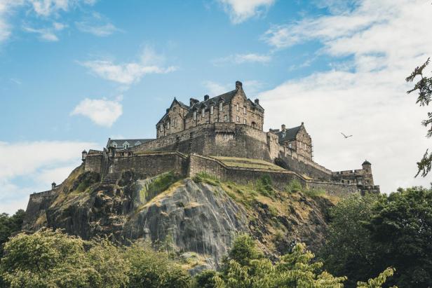 Edinburgh Castle thront auf einem Felsen unter blauem Himmel.