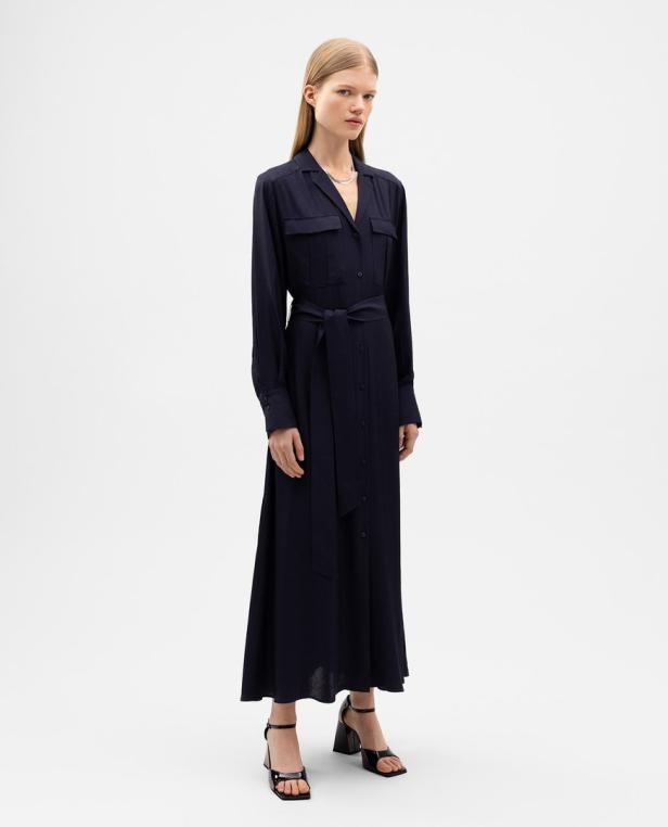 Eine Frau trägt ein dunkelblaues, langes Hemdkleid mit Gürtel und schwarze Sandalen.