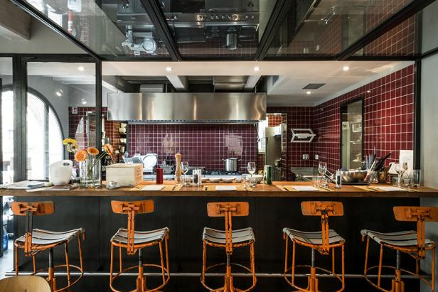 Ein Tresen mit Barhockern vor einer Restaurantküche mit rotem Fliesenspiegel.