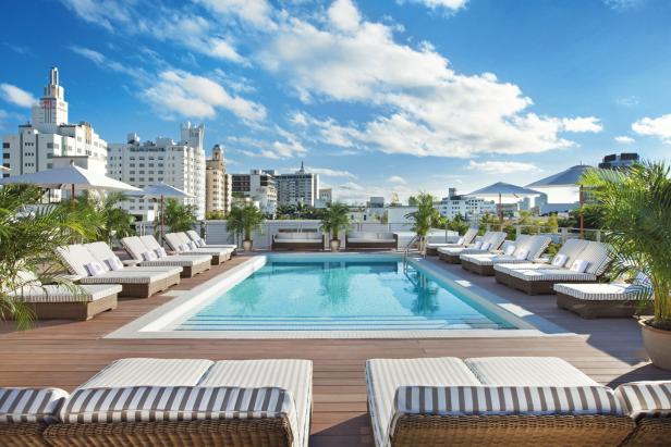 Ein Swimmingpool auf einer Dachterrasse mit Liegestühlen und Blick auf die Stadt.