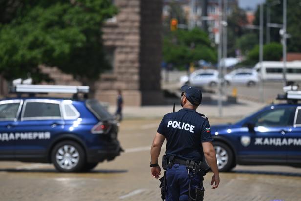 Ein Polizist steht auf einer Straße mit Polizeiautos im Hintergrund.