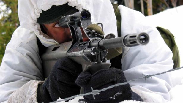 Ein Soldat zielt mit einem Gewehr im Schnee hinter einem Stacheldrahtzaun.