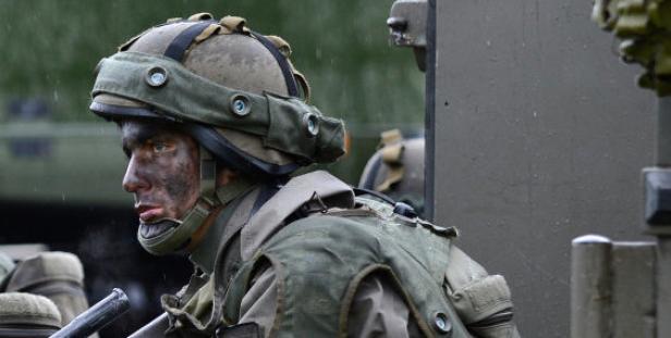 Ein Soldat mit Tarnfarbe im Gesicht und Helm steht neben einem Militärfahrzeug.