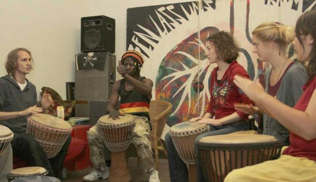 Eine Gruppe von Menschen spielt gemeinsam auf Djemben in einem Raum.