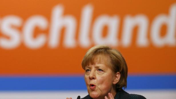 Angela Merkel spricht vor einem orangefarbenen Hintergrund mit dem Schriftzug „schland“.