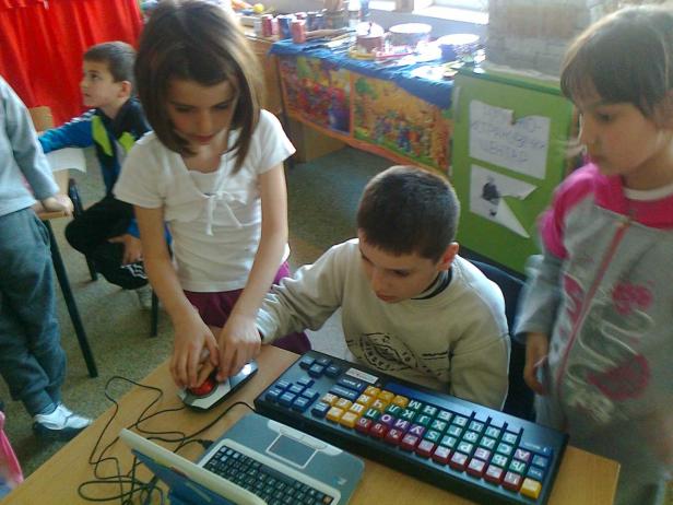 Kinder arbeiten mit einem speziellen Keyboard und einer Trackball-Maus an einem Laptop.