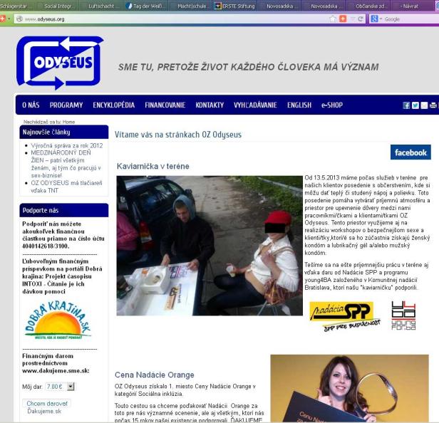 Ein Mann und eine Frau sitzen an einem Tisch im Freien; im Hintergrund ein Auto.