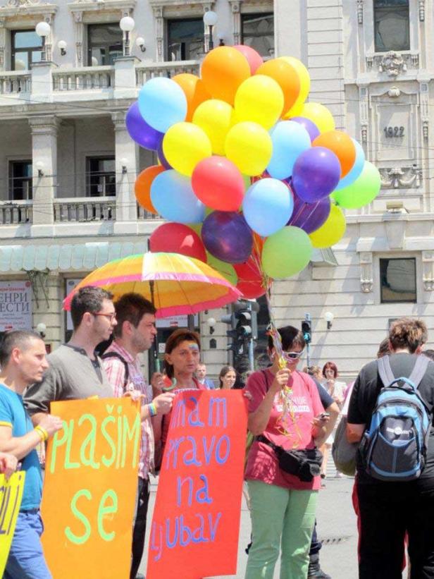 Eine Gruppe von Menschen demonstriert mit bunten Ballons und Schildern für die Rechte von LGBT-Personen.