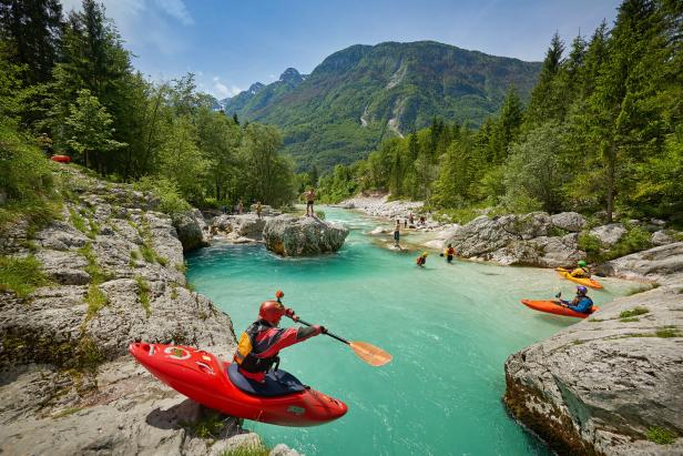 Ein Kajakfahrer auf einem türkisfarbenen Fluss inmitten einer Berglandschaft.