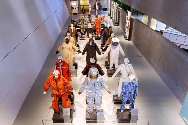 Eine Ausstellung verschiedener Schutzanzüge auf Schaufensterpuppen in einem Museum.