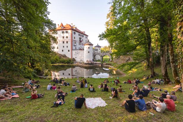 Zahlreiche Menschen sitzen auf einer Wiese vor Schloss Orth in Österreich.