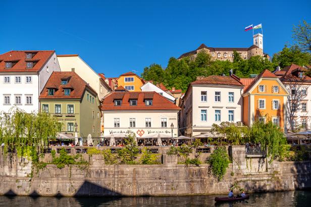 Blick auf Ljubljana mit der Burg im Hintergrund und einem Paar im Kanu im Fluss.