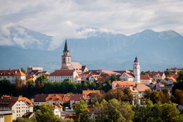Blick auf eine Stadt mit roten Dächern und Kirchtürmen vor einer Bergkulisse.