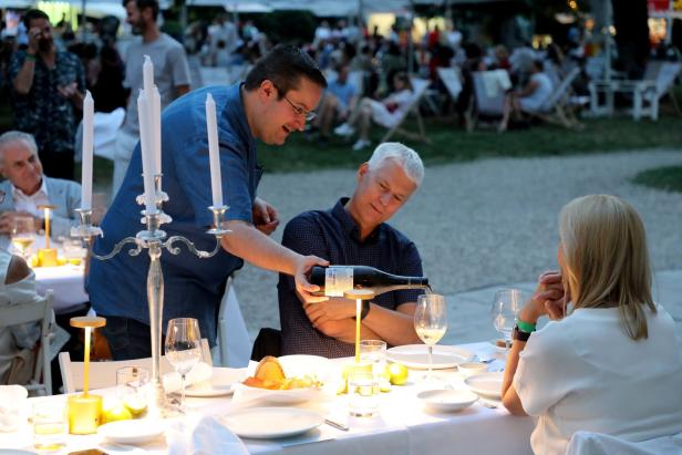 Ein Mann schenkt bei einem Abendessen im Freien Wein in ein Glas.