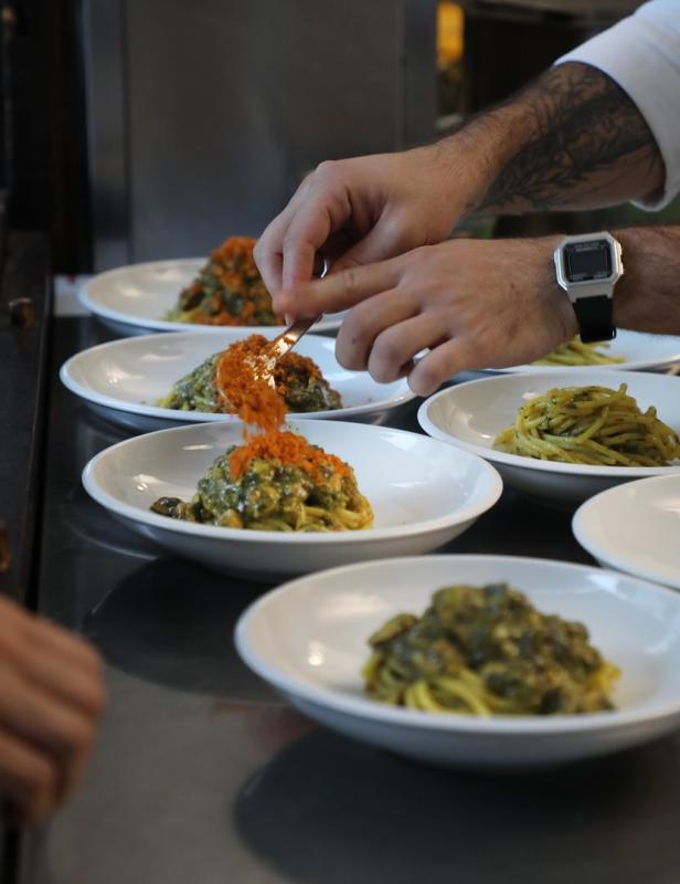Ein Koch garniert Teller mit Spaghetti und einer orangefarbenen Zutat.