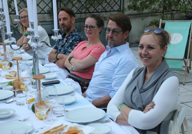 Mehrere Personen sitzen an einem gedeckten Tisch im Freien.