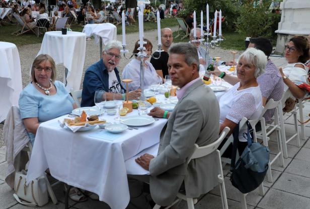 Eine Gruppe von Menschen sitzt an einem Tisch im Freien und isst zu Abend.