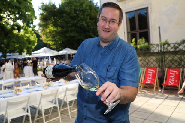 Ein Mann schenkt Weißwein in ein Glas im Freien ein.
