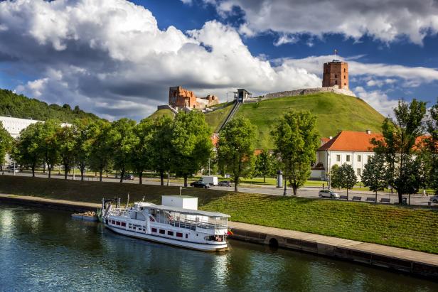 Ein Ausflugsschiff liegt am Flussufer von Vilnius, im Hintergrund der Gediminas-Turm.