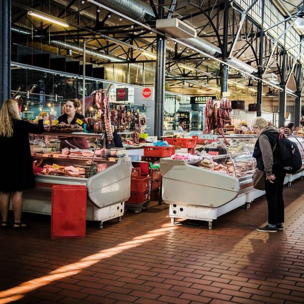 In einer Markthalle kaufen Menschen an verschiedenen Fleischständen ein.
