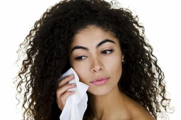 Eine Frau mit lockigem Haar reinigt ihr Gesicht mit einem Tuch.