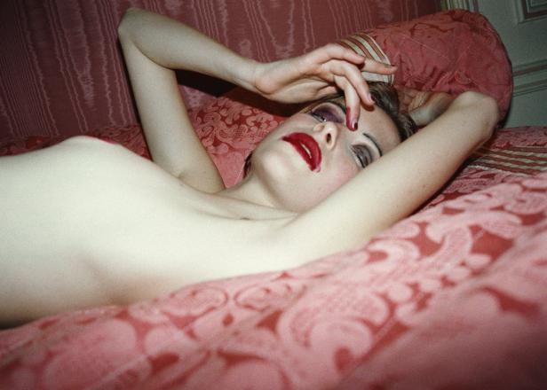 Eine Frau mit rotem Lippenstift liegt auf einem rosa gemusterten Bett.