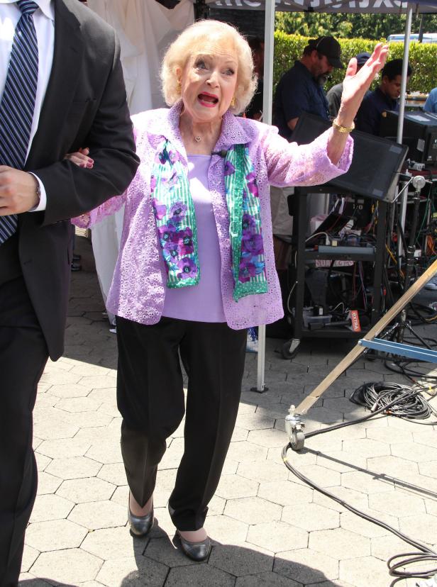 Betty White wird von einem Mann gestützt, während sie im Freien spricht.