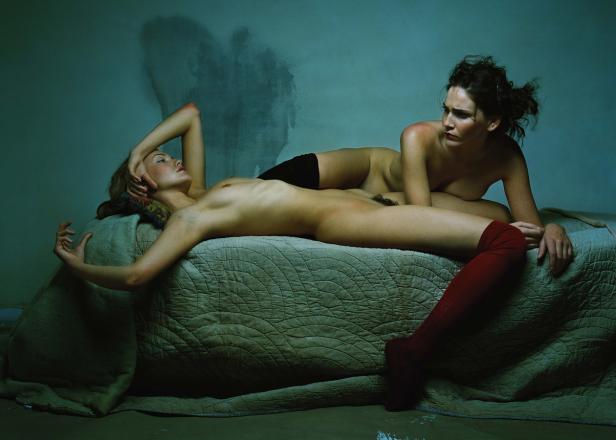 Zwei Frauen liegen auf einem Bett in einem spärlich beleuchteten Raum.